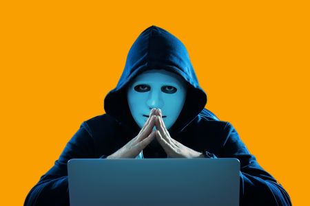 anonymous-online-presence A person in a blue hoodie sitting in front of a laptop with hands clasped, face obscured by a blue square, against an orange background.
