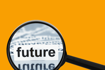 focusing-on-the-future A magnifying glass focused on the word “future” printed in bold letters, with blurred text in the background, against a vibrant orange backdrop.