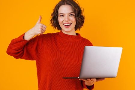 person-giving-thumbs-up-while-holding-laptop A person in a red sweater holding a laptop with one hand and giving a thumbs up with the other against an orange background, face obscured by a brown rectangle.